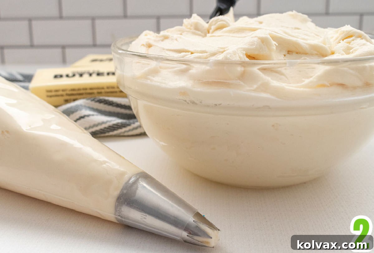 A clear glass bowl filled with fluffy homemade buttercream frosting sits next to a piping bag already filled with frosting, ready for decorating.