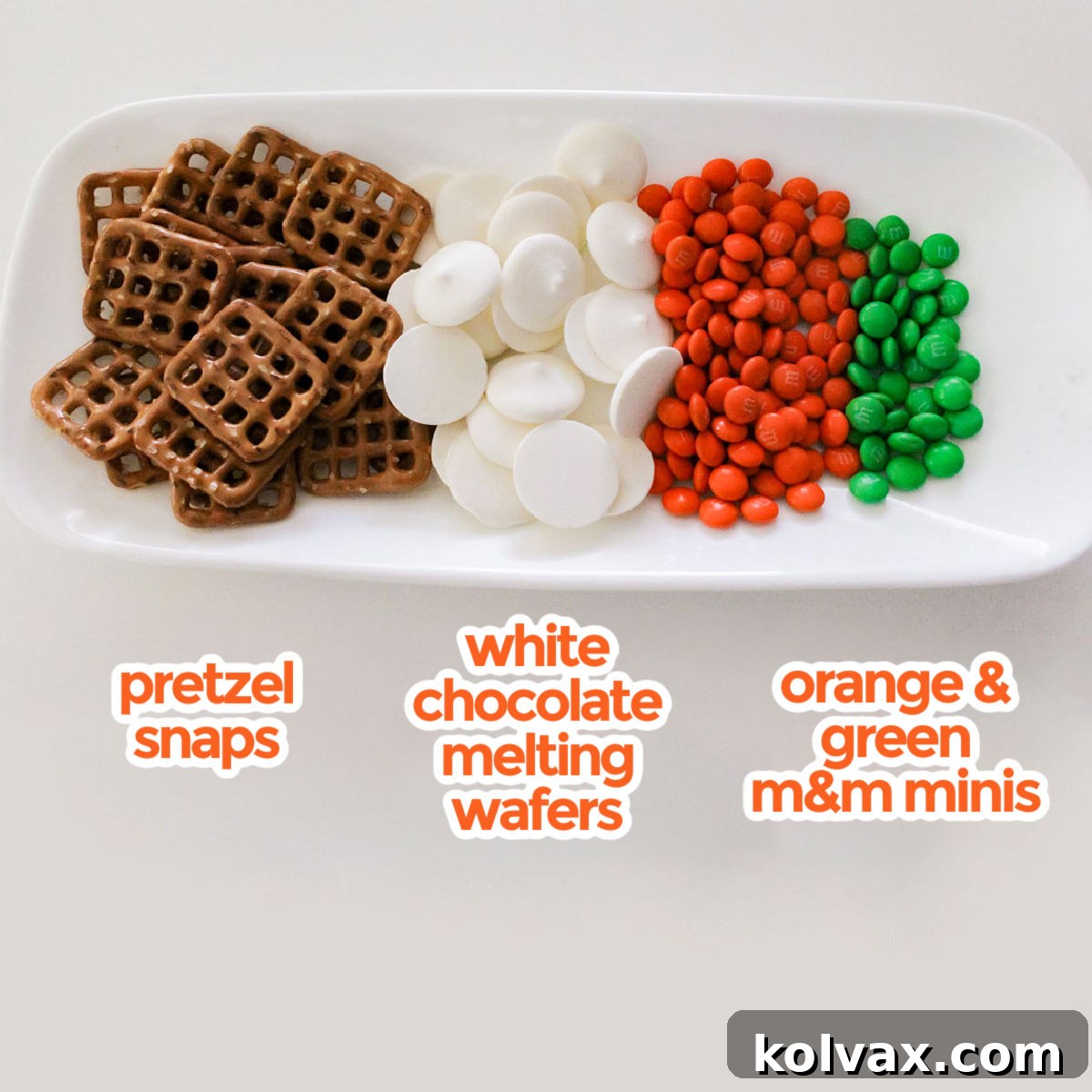 A visual display of all the necessary ingredients for crafting Easter Bunny Carrot Pretzel Bites, featuring square Pretzel Snaps, creamy White Chocolate Melting Wafers, and colorful Green and Orange Mini M&M's.
