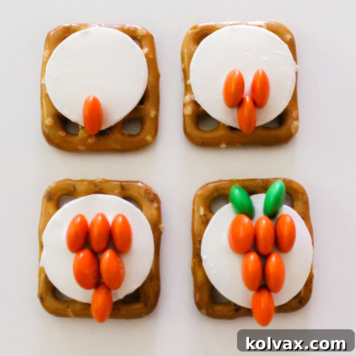 A detailed close-up image demonstrating the precise technique for arranging orange and green mini M&M's to construct a small, vibrant carrot shape on a melted white chocolate base.