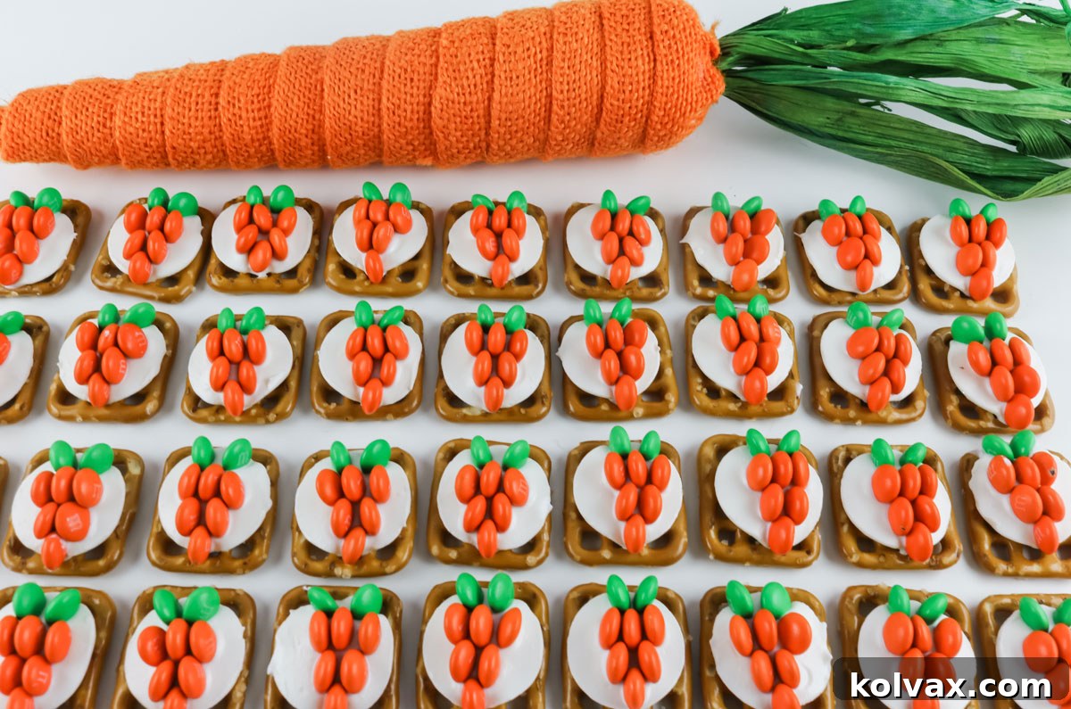 Neatly organized rows of finished Easter Bunny Carrot Pretzel Bites are displayed on a clean white surface, positioned in front of a soft fabric carrot decoration.