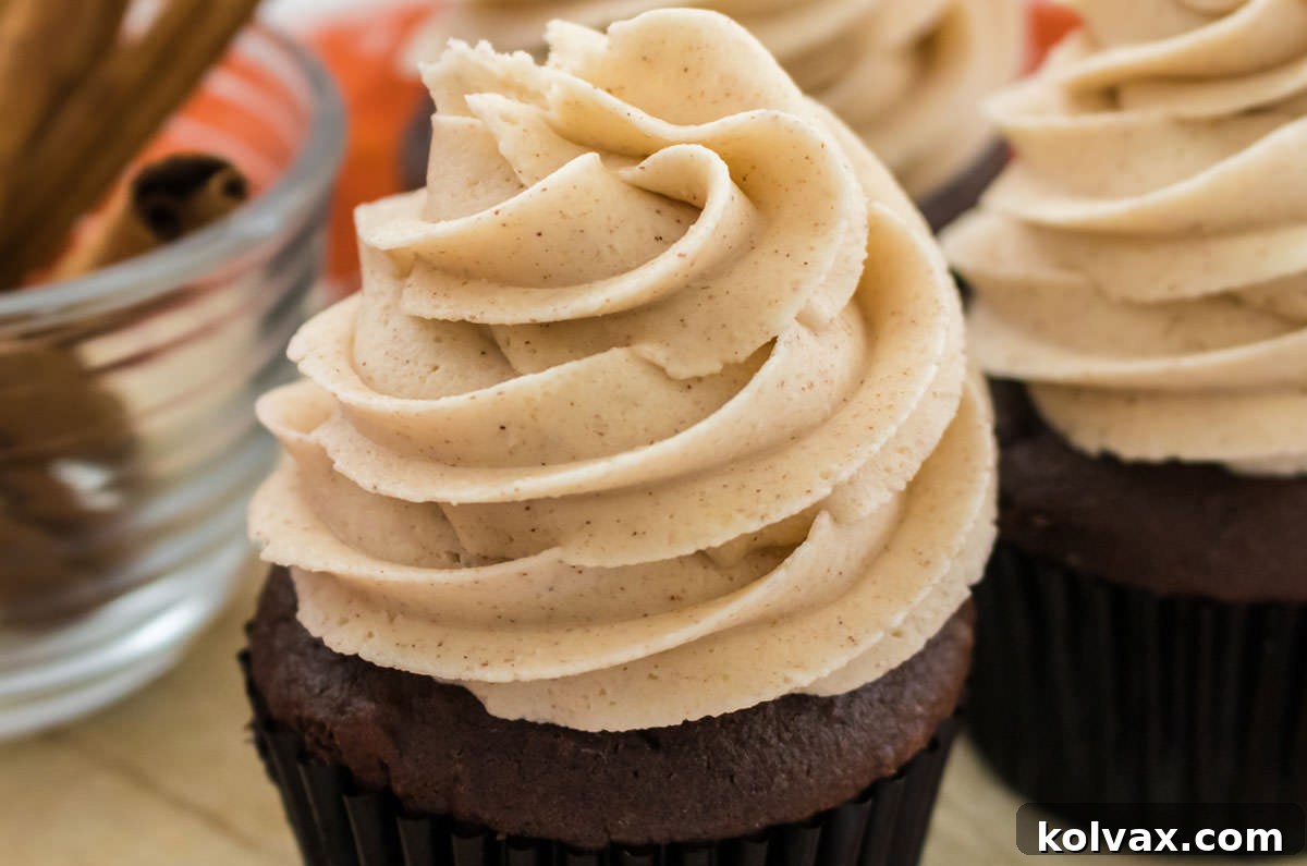 Heavenly Cinnamon Buttercream 2 Three chocolate cupcakes elegantly topped with a generous swirl of The Best Cinnamon Buttercream Frosting, arranged on a rustic wooden board. A small bowl of fragrant cinnamon sticks sits beside them, hinting at the delightful spice within the frosting.