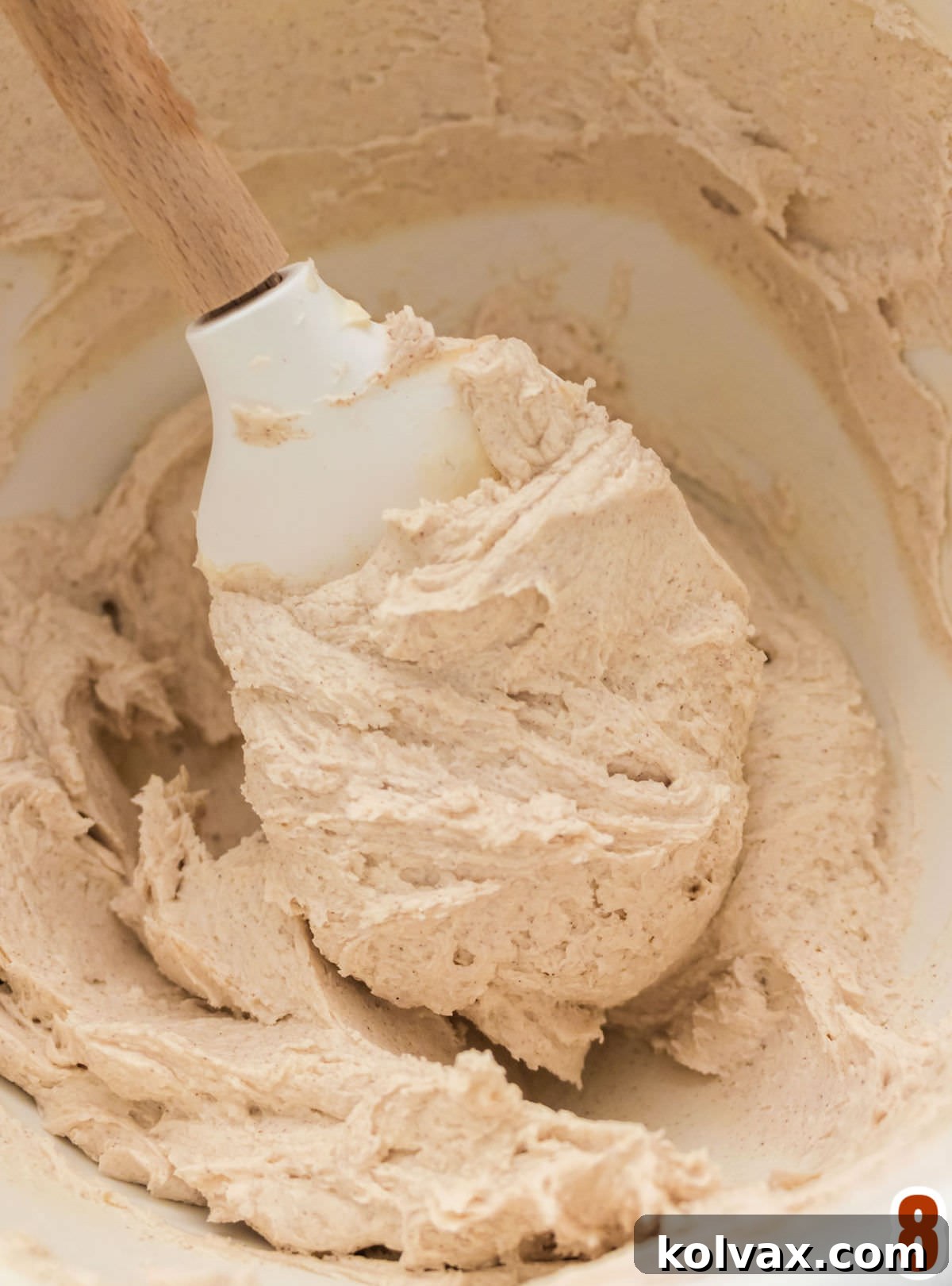 Heavenly Cinnamon Buttercream 5 A close-up view of a mixing bowl brimming with freshly made, velvety Cinnamon Icing. A pristine white wooden spoon rests inside, ready for a taste test, highlighting the smooth and creamy texture of the frosting.