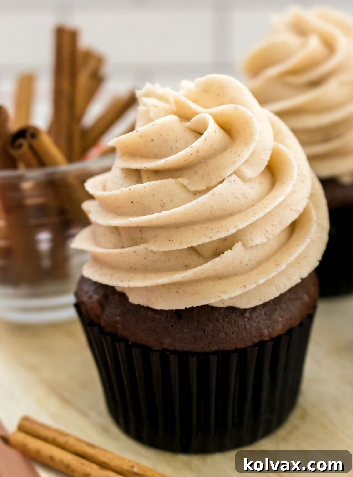 Heavenly Cinnamon Buttercream 7 A delightful close-up of a perfectly frosted chocolate cupcake crowned with The Best Cinnamon Buttercream Frosting, sitting elegantly on a cutting board next to a small ramekin filled with aromatic cinnamon sticks. The image emphasizes the rich flavors and inviting presentation.