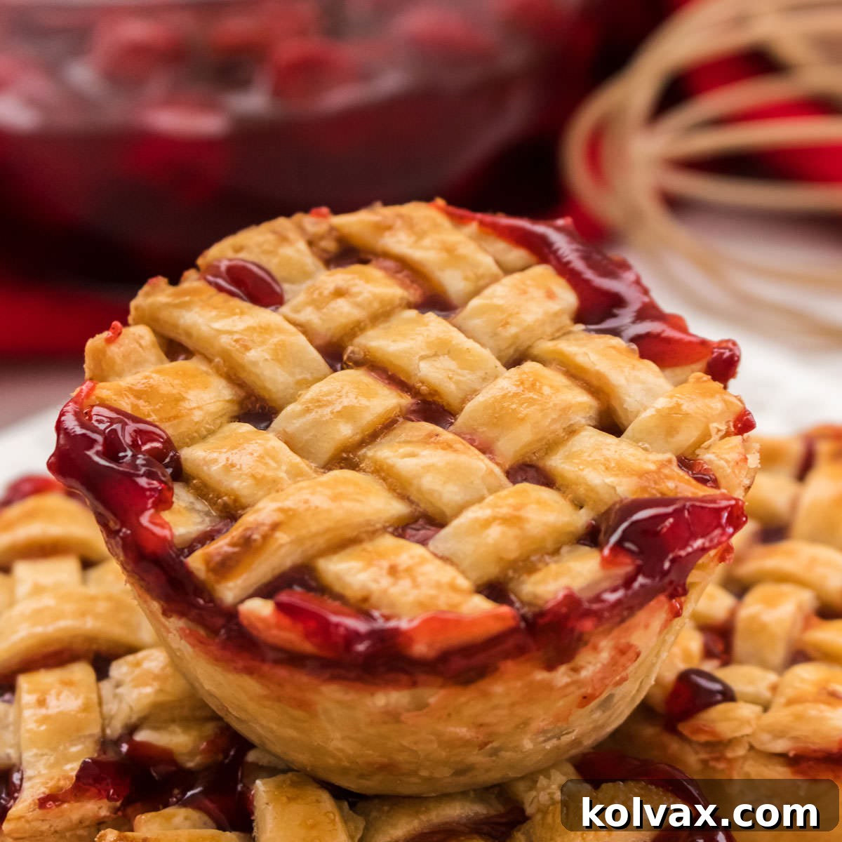 Closeup on a Mini Cherry Pie with a delicate lattice pie crust top, sitting on a pile of other pies, highlighting its appealing texture and color.