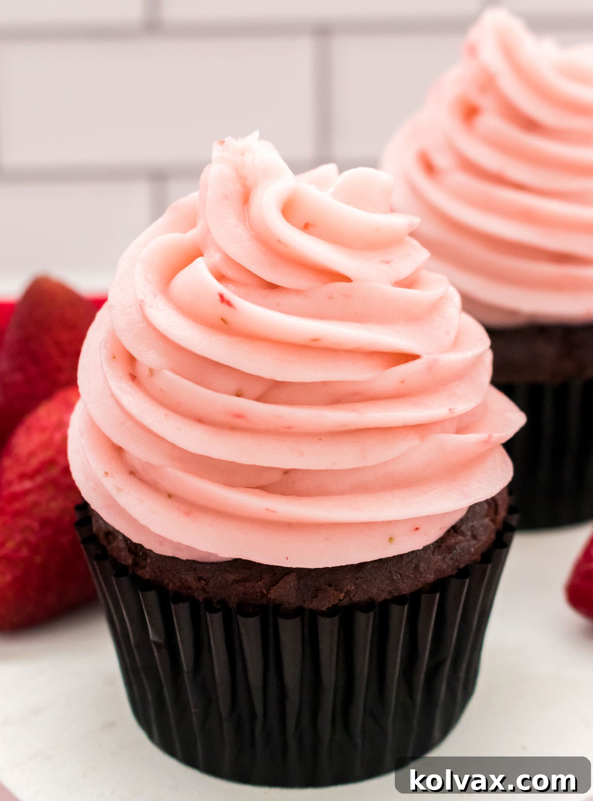 Two rich chocolate cupcakes adorned with generous swirls of homemade strawberry buttercream frosting, artfully arranged next to a stack of fresh, ripe strawberries.