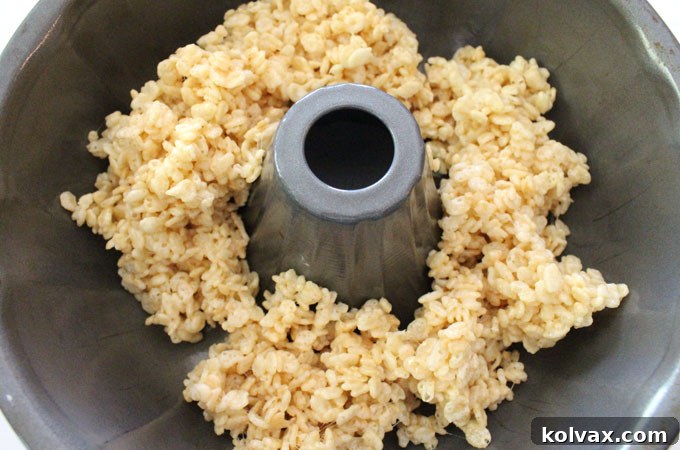 Creating the first layer of the Ombre Rice Krispie Cake - The initial step of carefully pressing the lightest shade of Rice Krispie Treat mixture into a greased bundt pan, forming the base of your stunning ombre dessert. Precision and care are key here.