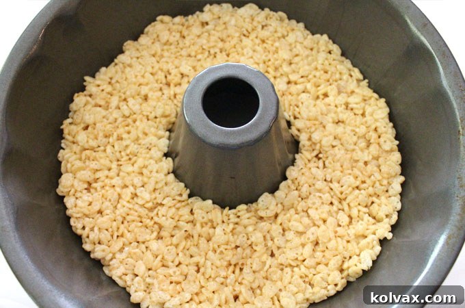 Press the Rice Krispie Treat mixture into the bundt pan - Demonstrates the important technique of firmly, yet gently, pressing each layer of Rice Krispie Treat mixture into the bundt pan to create a solid, even foundation for your Ombre Rice Krispie Cake.