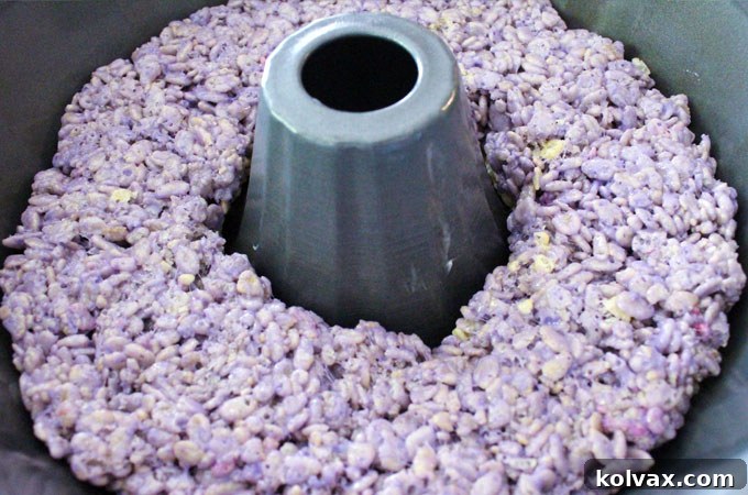Continue adding layers of the color Rice Krispie Treat mixture - A progress shot showing multiple vibrant layers of Rice Krispie Treats already added to the bundt pan, illustrating the gradual build-up of the ombre effect for the cake.