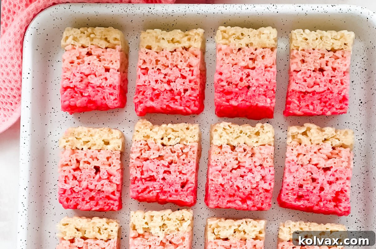 An overhead shot showcasing a beautiful arrangement of Ombre Rice Krispie Treats, cut into neat gradient slices and perfectly aligned in rows within a crisp white cookie sheet.