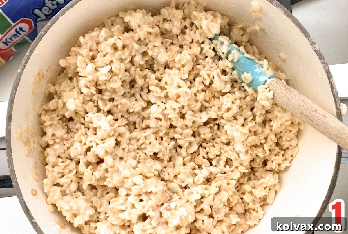 White sauce pan filled with warm Rice Krispie Treat mixture and a white wooden spoon.