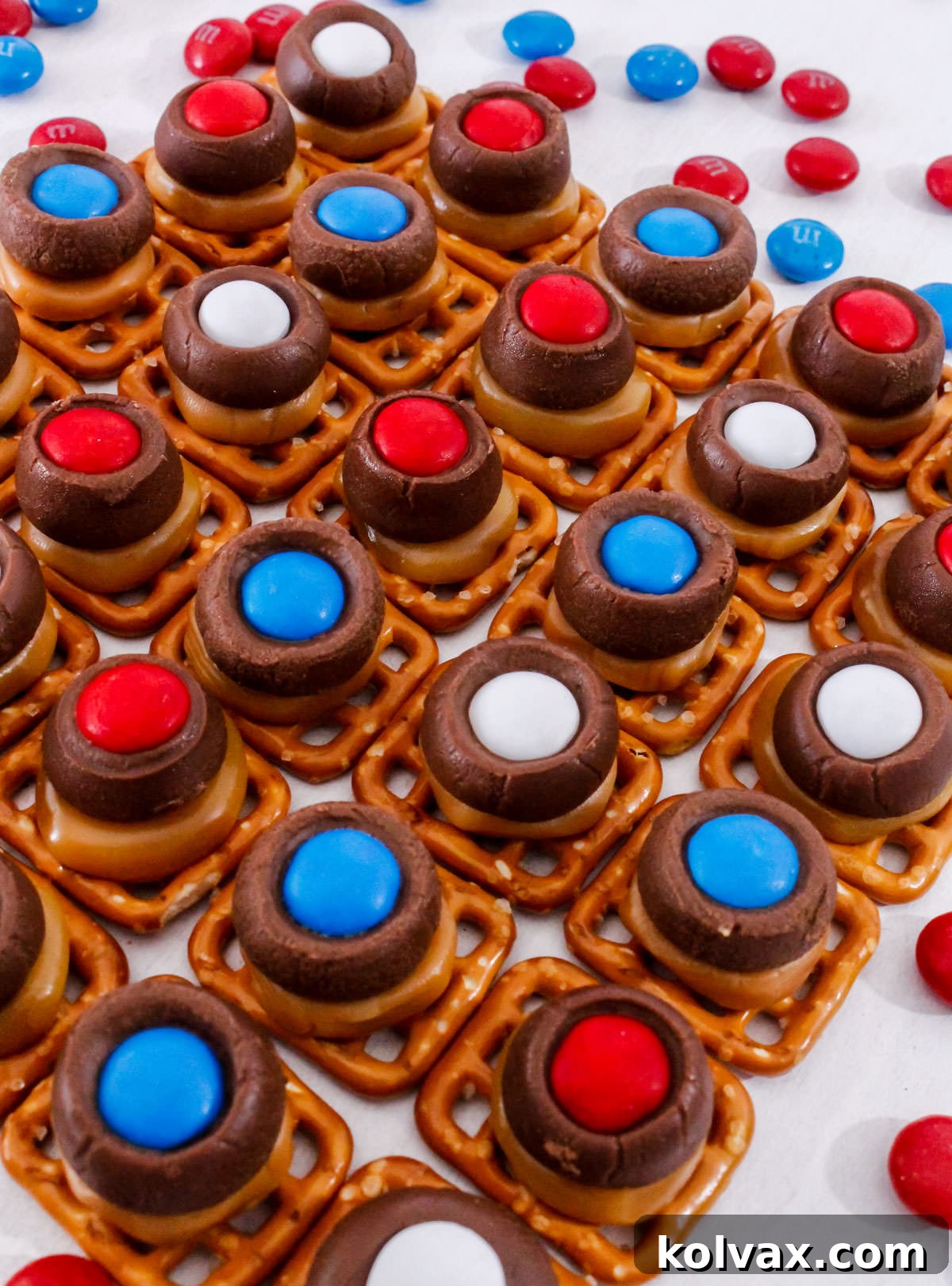 An overhead shot of red, white, and blue Patriotic Caramel Pretzel Bites arranged in an attractive diamond pattern on a pristine white surface, highlighting their festive colors and neat presentation.