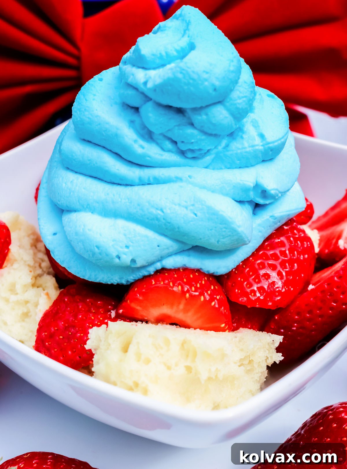 Closeup of a white bowl filled with Red White and Blue Strawberry Shortcake sitting on a white table in front of a big red bow.