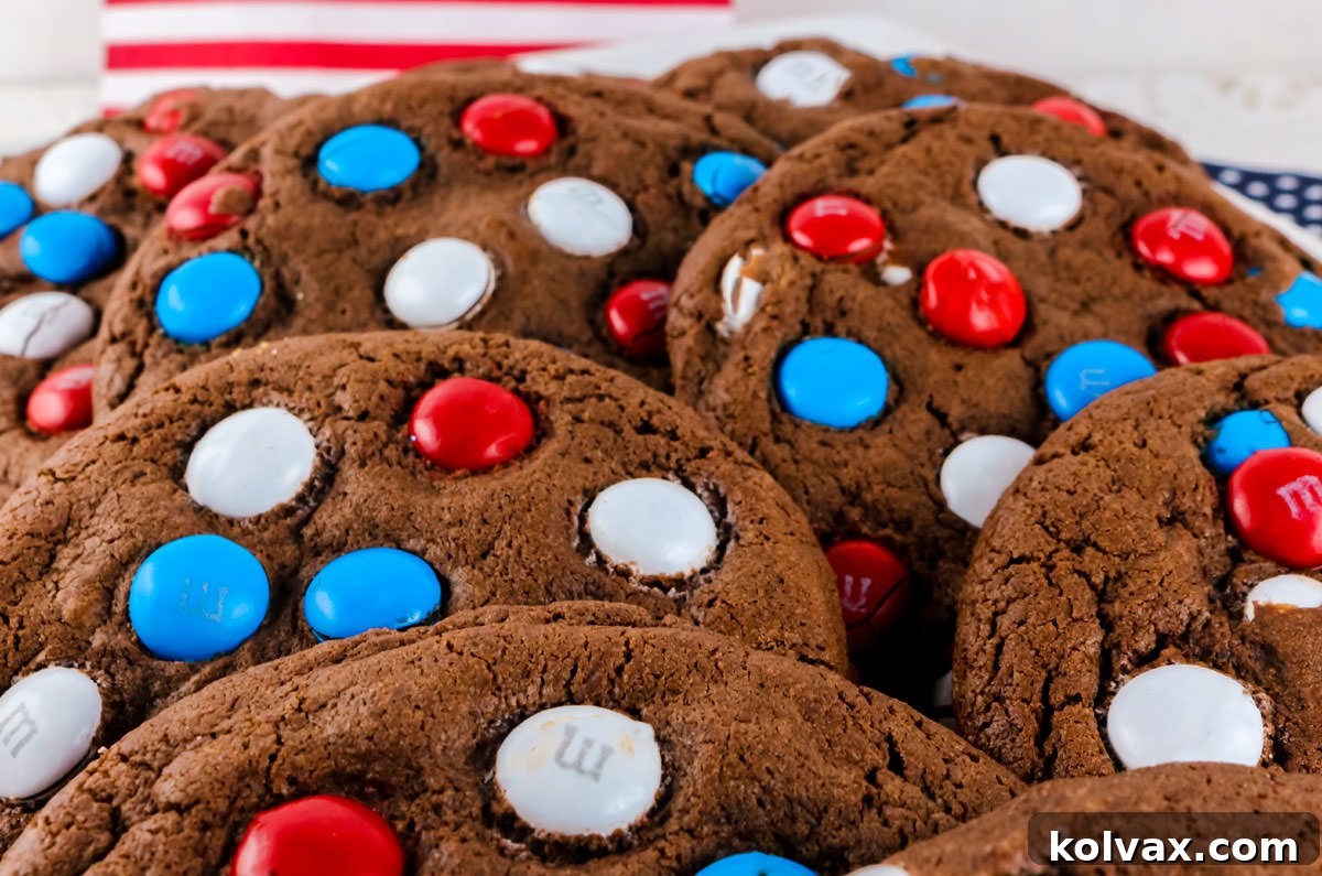 Closeup on a bunch of Red White and Blue M&M Cookies lying flat on a white serving platter in front of a white background and 4th of July decorations.