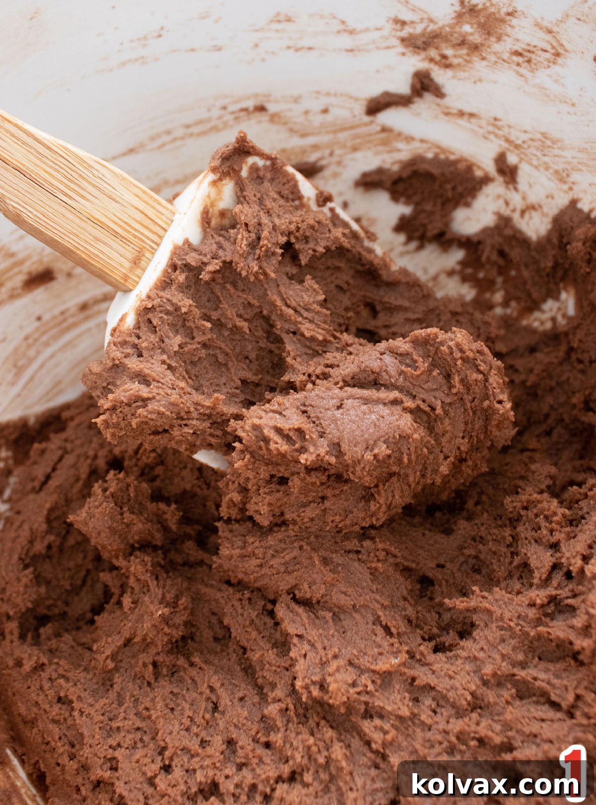 Closeup on a white mixing bowl filled with Chocolate Cookie dough and a white wooden spoon.