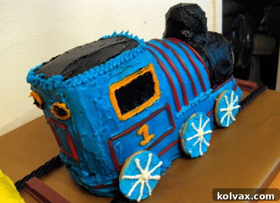 Partially decorated Thomas the Train cake, showing the initial blue frosting and red licorice detailing, set up for further decoration.