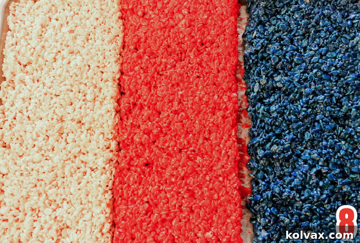 Closeup shot of all three distinct colors of Rice Krispie Treat mixture neatly pressed into separate sections of a large cookie sheet.