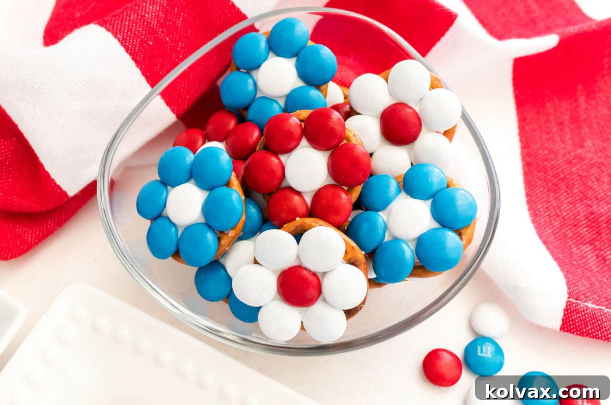 Closeup on a glass dish filled with Patriotic Flower Pretzel Bites sitting on a white table in front of an American Flag kitchen towel.