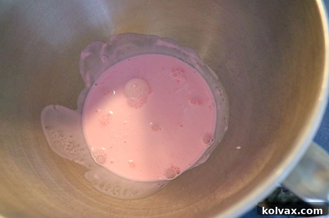 Colored heavy whipping cream being poured into a chilled metal mixing bowl, ready for whipping.
