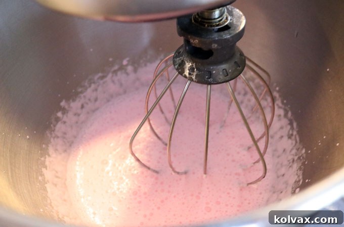 A stand mixer whisking colored heavy whipping cream and powdered sugar, creating fluffy homemade whipped cream.