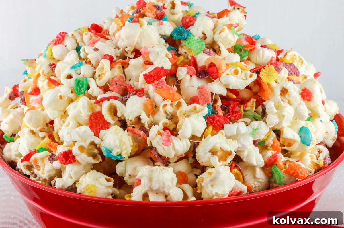 Closeup on a red serving bowl filled with Fruity Pebbles Popcorn sitting on a white table.