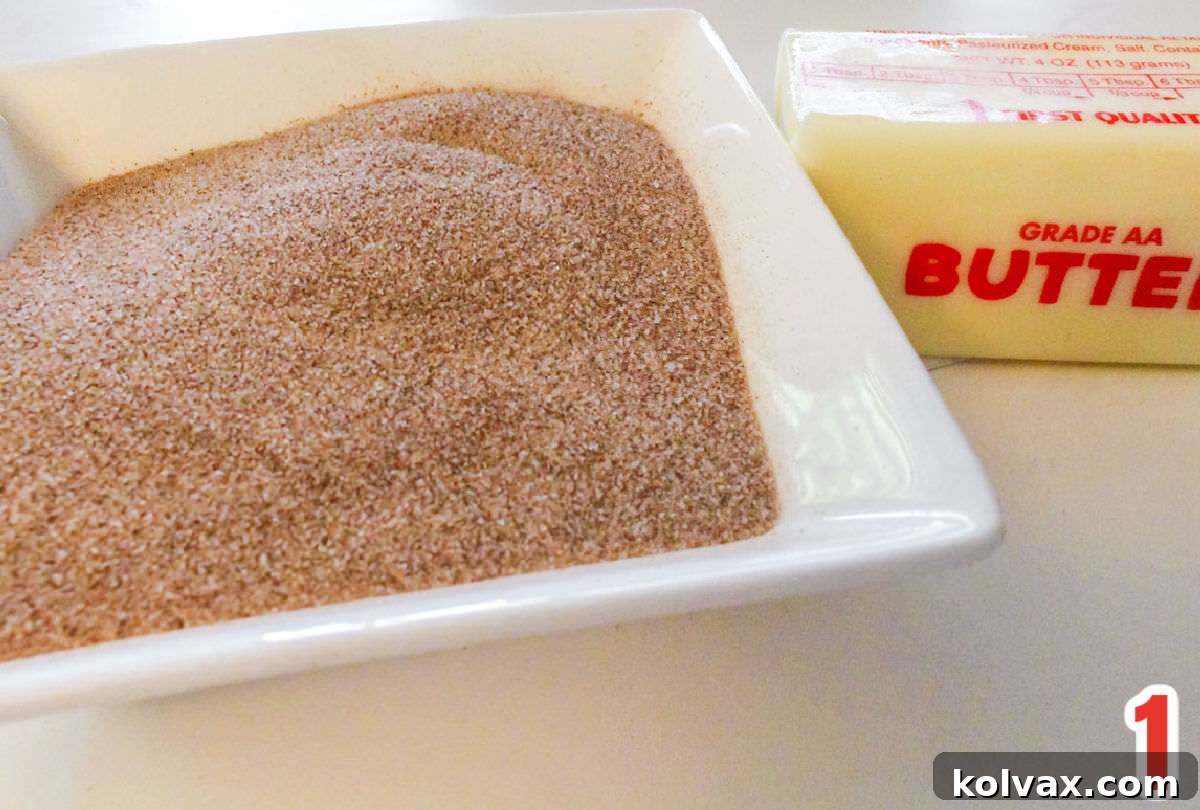 A small white ramekin filled with golden cinnamon sugar, positioned beside a stick of butter, ready for use.