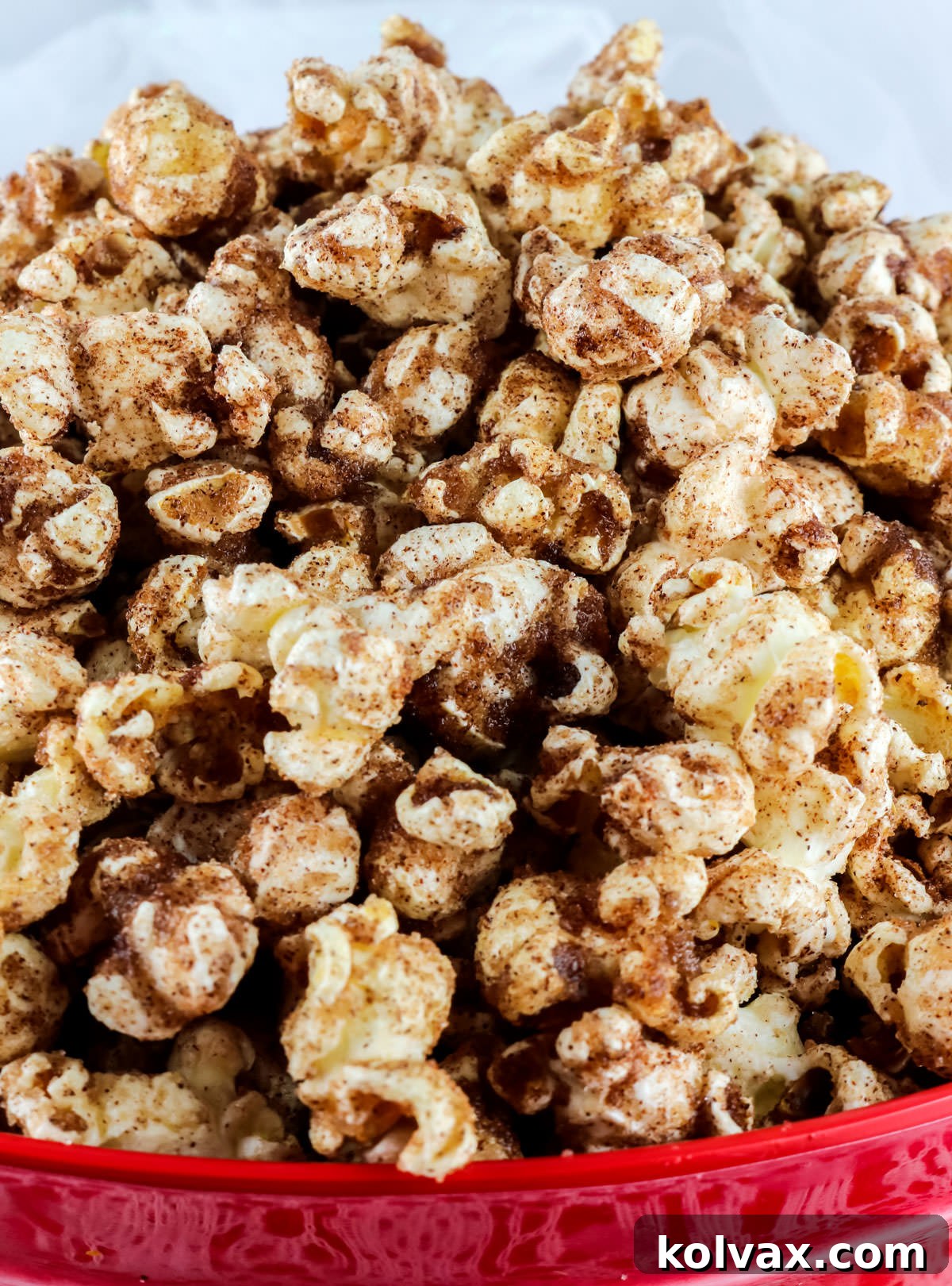 A close-up shot of a large, rustic red bowl overflowing with golden Cinnamon Toast Popcorn, perfectly coated in a sweet cinnamon sugar blend.