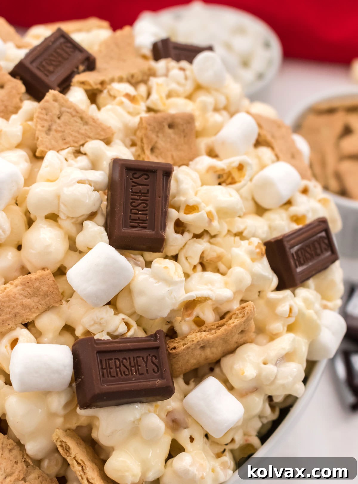 Campfire Crunch Popcorn 10 Closeup on a white bowl filled with S'mores Popcorn surrounded by ramekins filled with graham cracker pieces and mini marshmallows, ready for sharing.