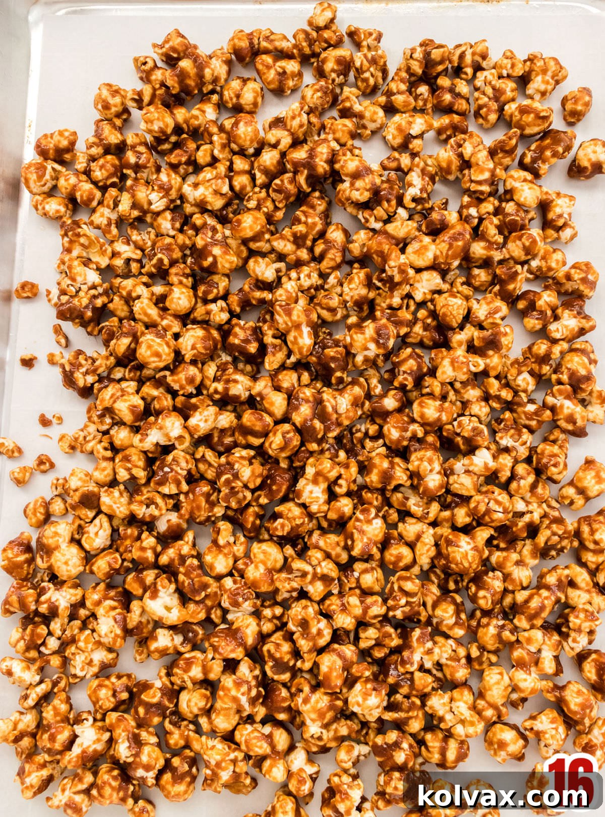 Closeup on a cookie sheet covered in parchment paper and filled with a batch of cooling Caramel Corn.
