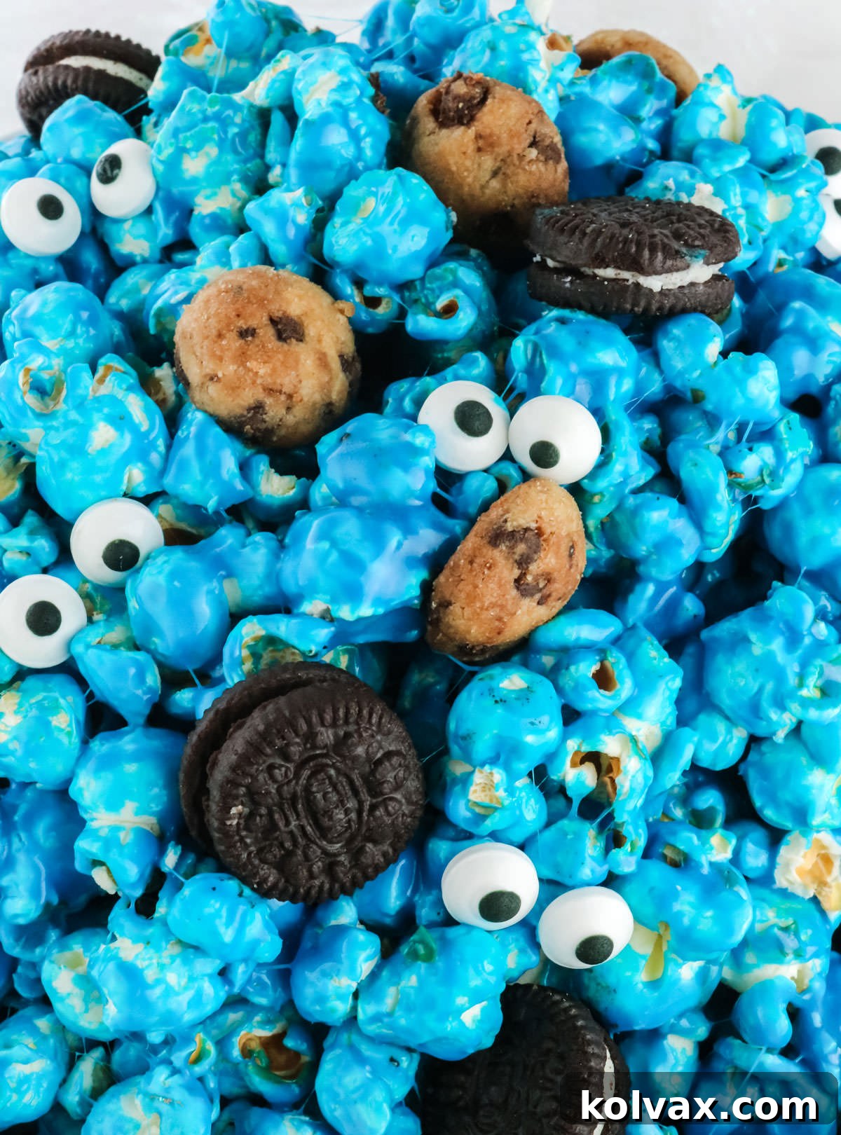 Closeup on a white serving bowl filled with blue Cookie Monster Popcorn, featuring mini cookies and candy eyes, on a light blue background.