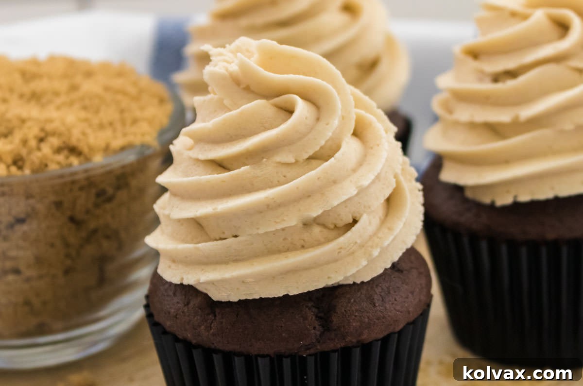Three decadent cupcakes lavishly topped with rich, creamy Brown Sugar Buttercream Frosting, sitting beside a glass bowl brimming with golden-brown sugar, highlighting the star ingredient.