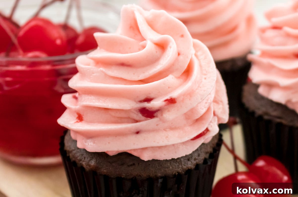 Three decadent cupcakes adorned with The Best Maraschino Cherry Buttercream Frosting, sitting beside a glass bowl brimming with bright red Maraschino Cherries.
