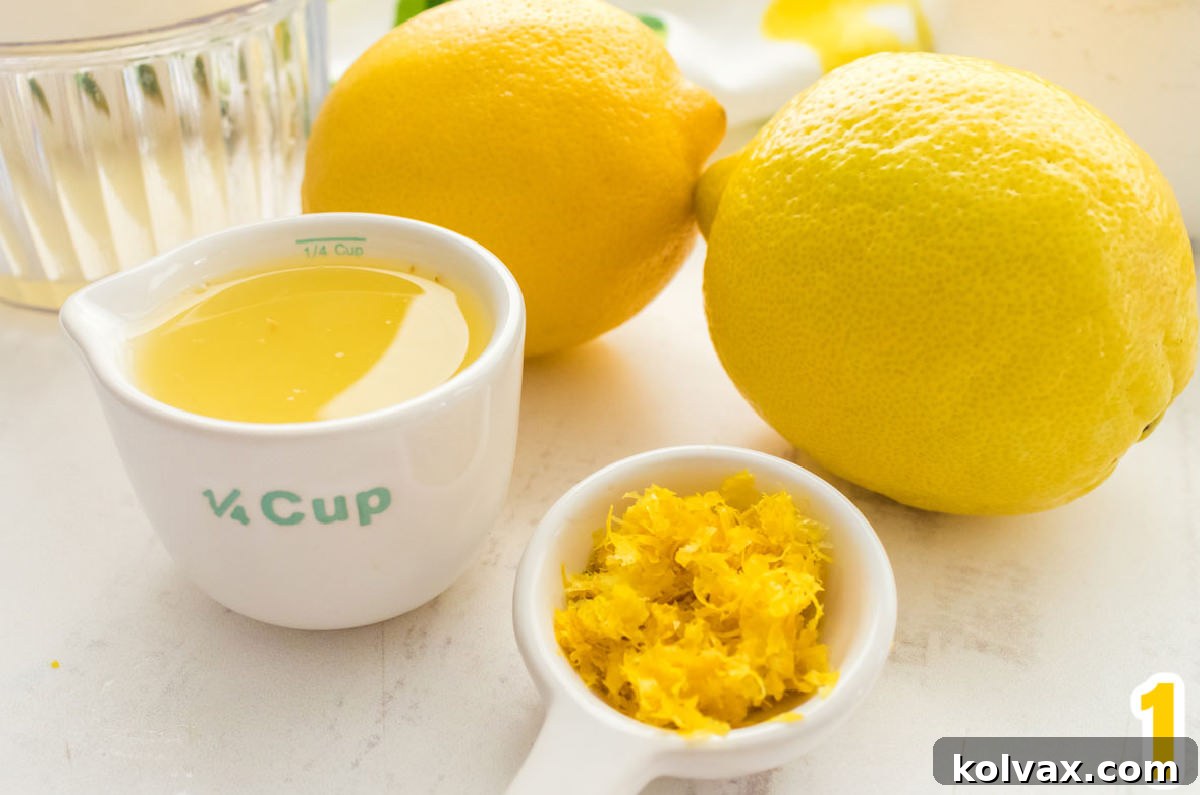 Close-up of fresh lemons, a measuring cup filled with freshly squeezed lemon juice, and finely grated lemon zest, highlighting the essential ingredients for lemon buttercream.