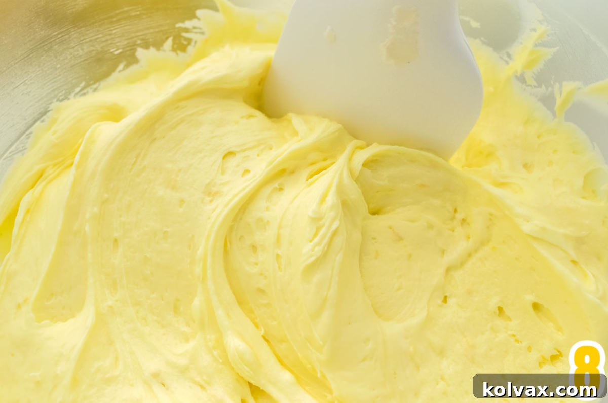 A mixing bowl full of freshly made Best Lemon Buttercream Frosting, shown with a white wooden spatula resting in it, ready for tasting.
