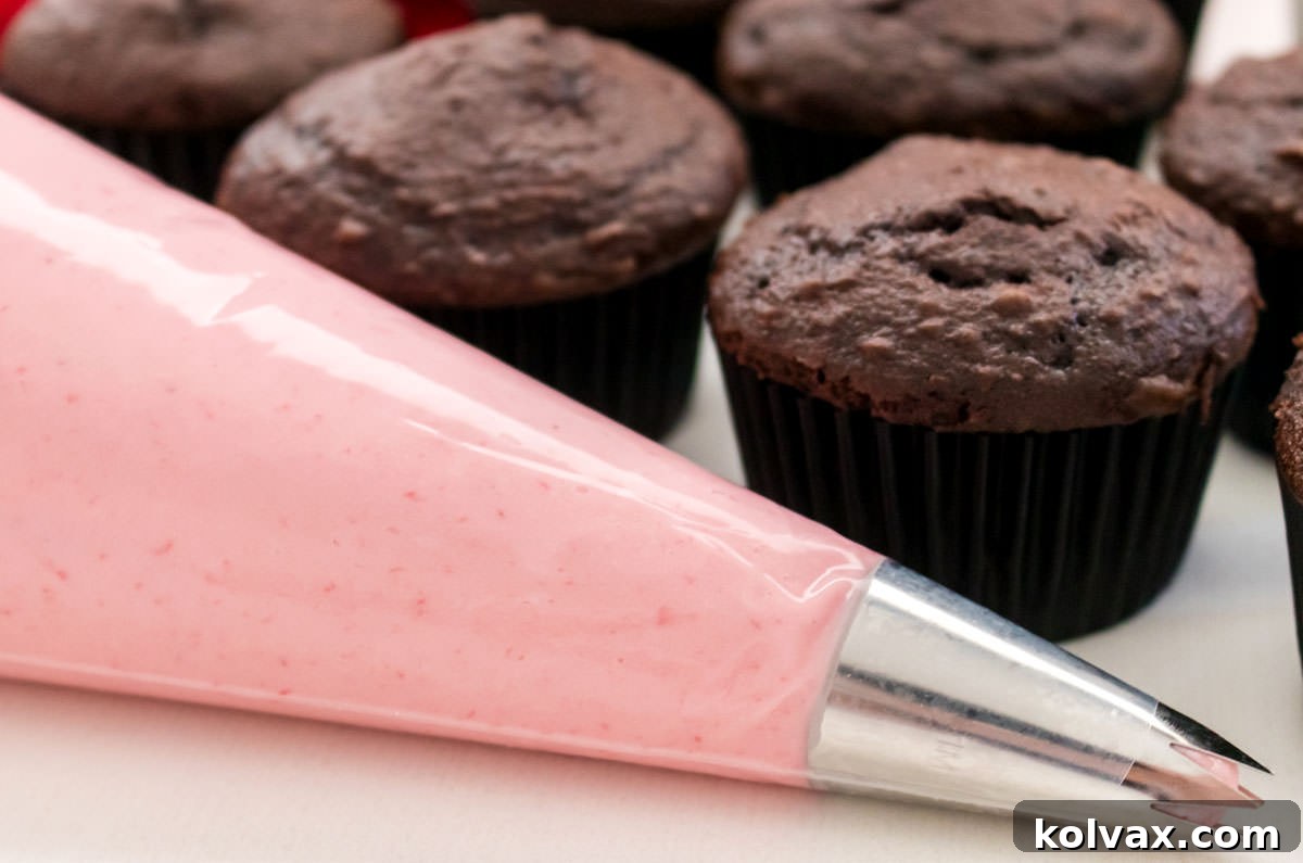 Decorating bag filled with fluffy raspberry frosting, ready to pipe onto chocolate cupcakes, emphasizing its versatility.
