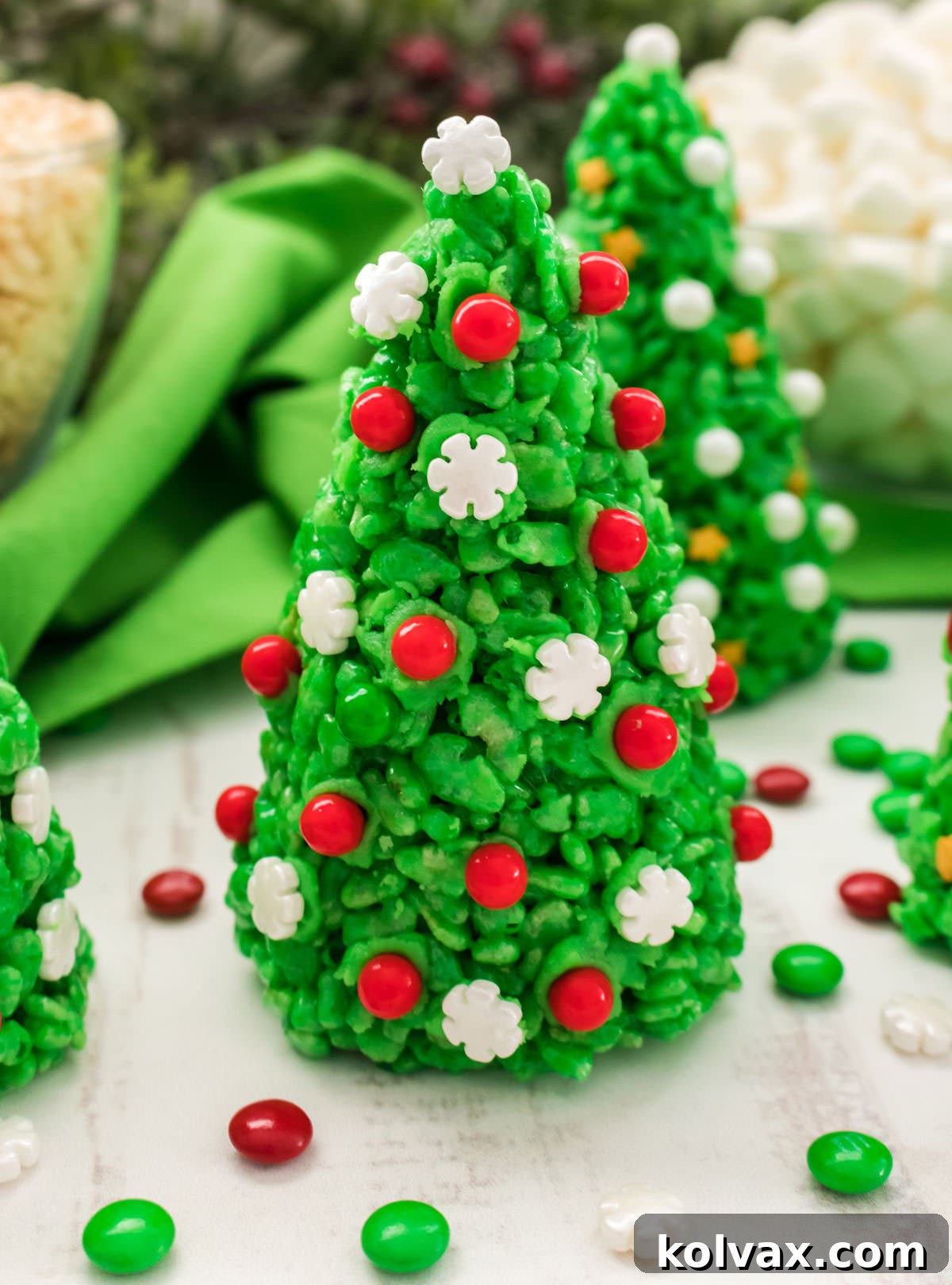 A close-up shot of a single, perfectly decorated Christmas Tree Rice Krispie Treat, surrounded by loose red and green M&M's and festive sprinkles on a white surface.