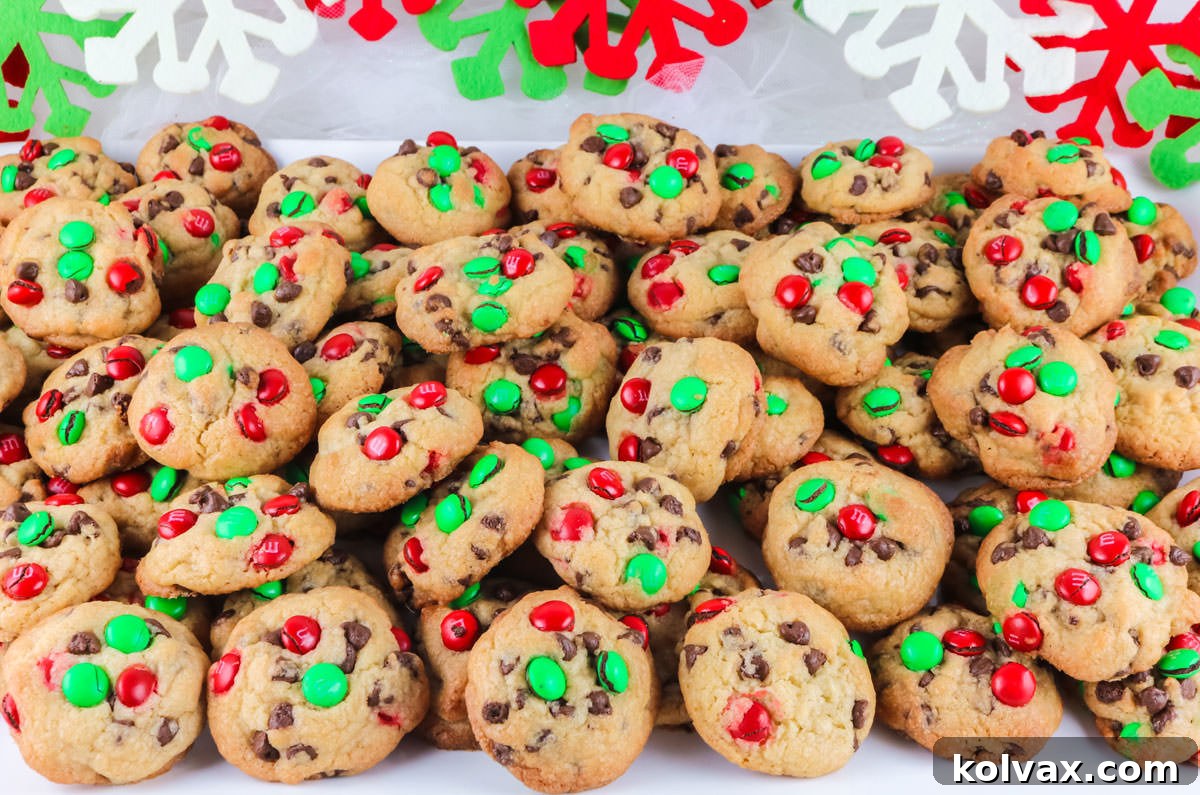 A festive white serving platter overflowing with perfectly baked Christmas M&M Mini Cookies, artfully arranged on a white table amidst charming Christmas decorations in the background.