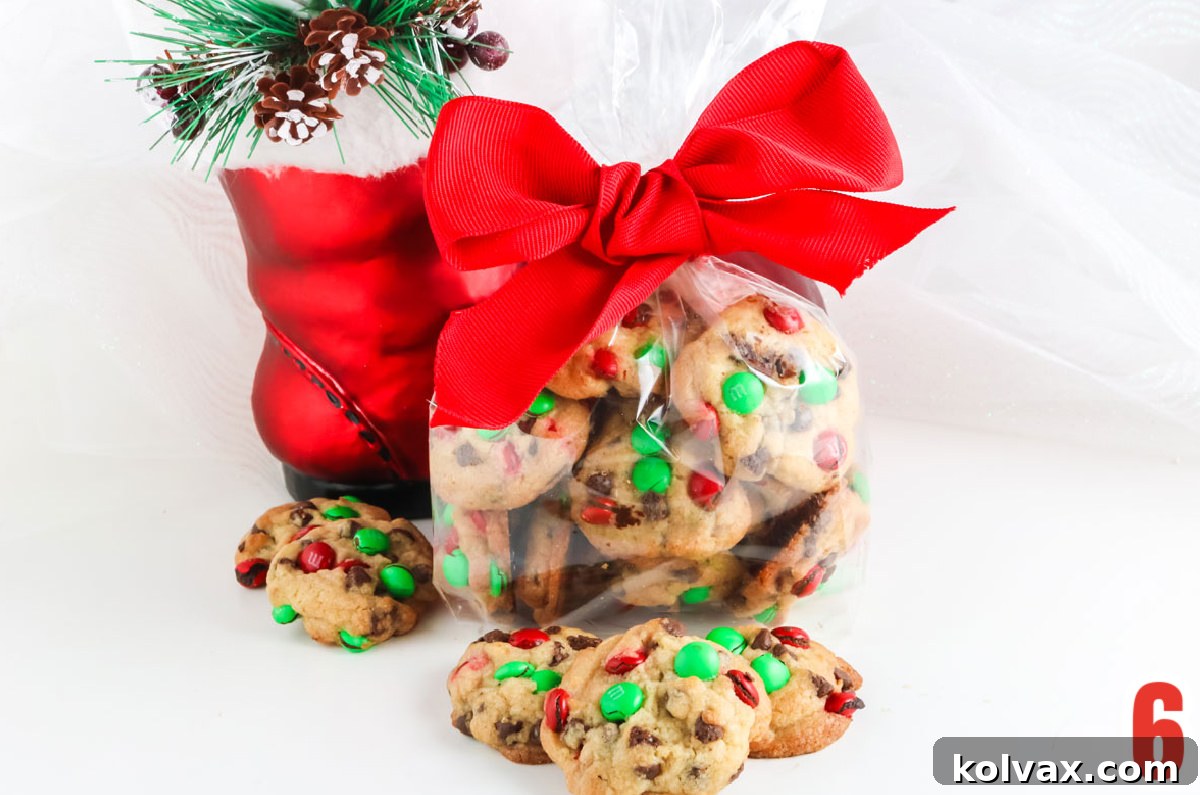A transparent gift bag brimming with festive Christmas M&M Mini Cookies, elegantly tied with a bright red ribbon, resting in front of a whimsical Santa Boot decoration.