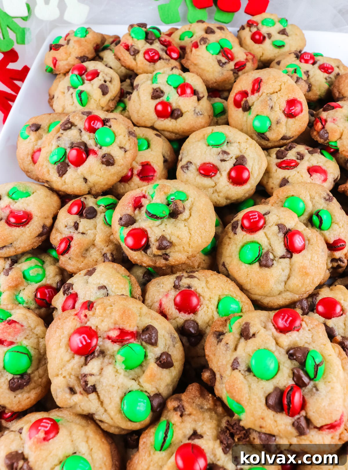 A vibrant close-up shot of a white serving plate, generously filled with a festive assortment of perfectly baked Christmas M&M Mini Cookies, highlighting their rich colors and inviting textures.