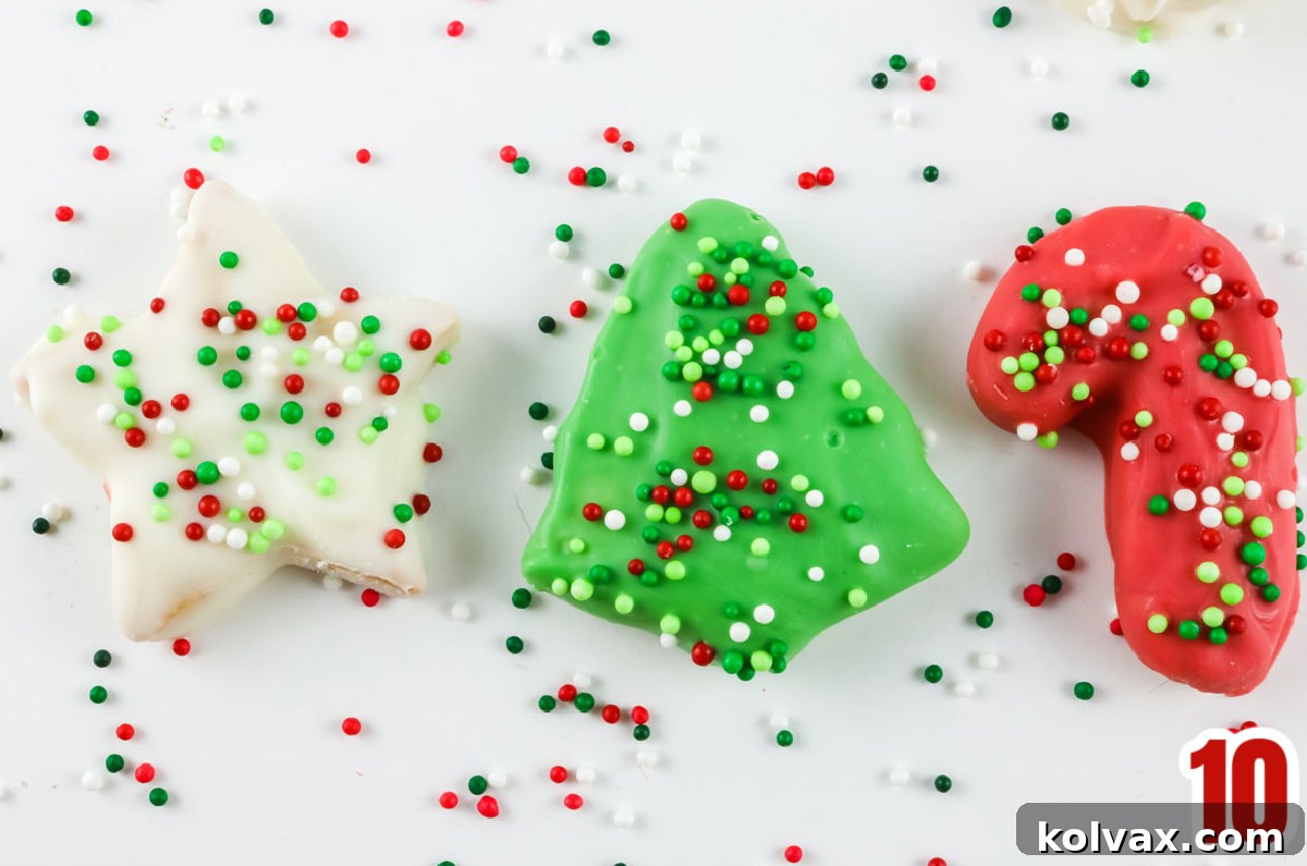 Three perfectly iced Christmas Circus Animal Cookies in red, green, and white, decorated with festive sprinkles, resting on a white surface surrounded by loose sprinkles.