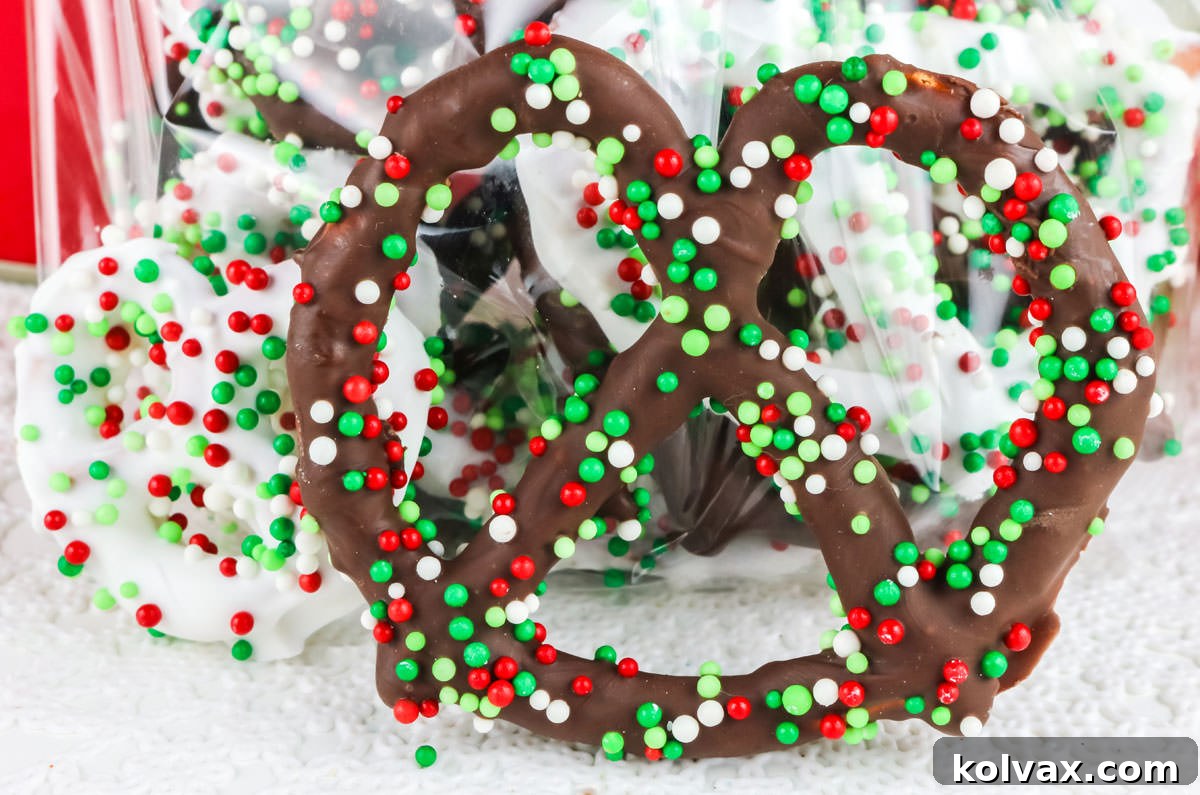Sweet and Salty Chocolate Pretzel Perfection 2 Closeup on two Homemade Chocolate Covered Pretzels sitting upright on a white table, adorned with festive sprinkles.