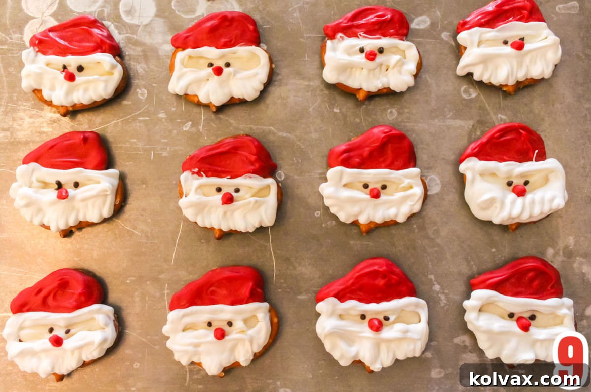 A dozen finished Santa Claus Pretzel Bites neatly arranged in rows on a reflective silver cookie sheet, ready for serving or packaging.