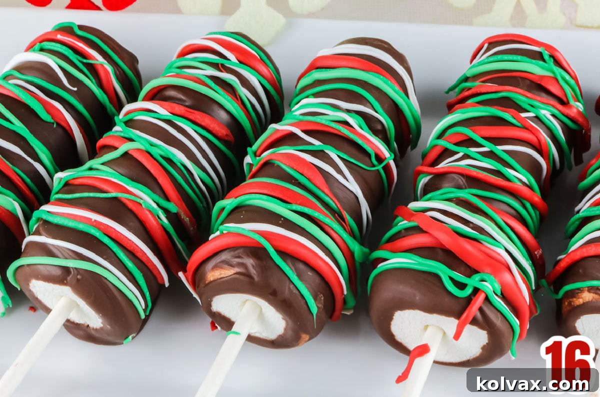 Closeup on five Christmas Marshmallow Pops laying on a white serving platter, beautifully decorated with candy melt drizzles.