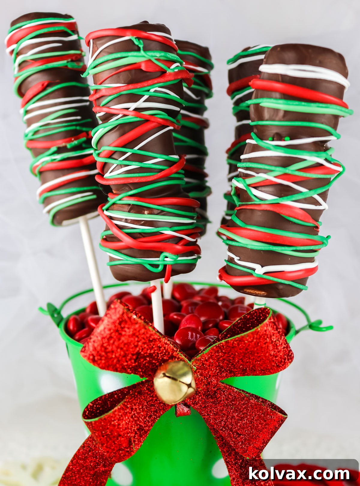 Five Christmas Marshmallow Pops sticking out of a green mini bucket with a red bow, ready for serving or gifting.