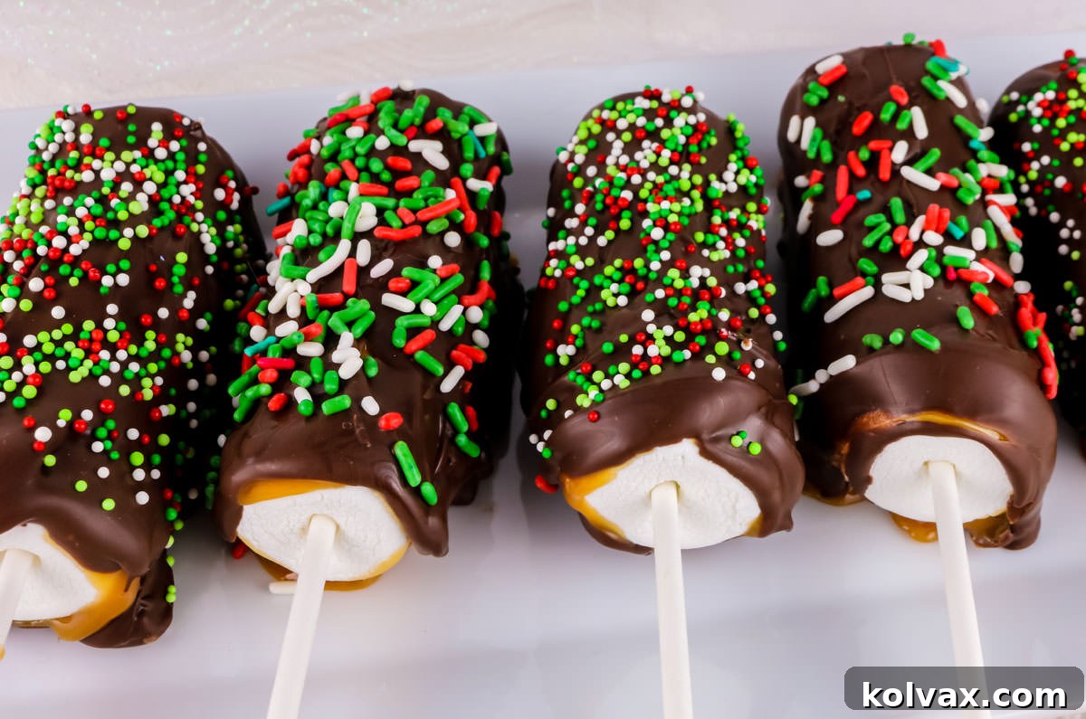 Five Christmas Caramel Marshmallow Pops on a white dish on a white table, adorned with festive sprinkles.