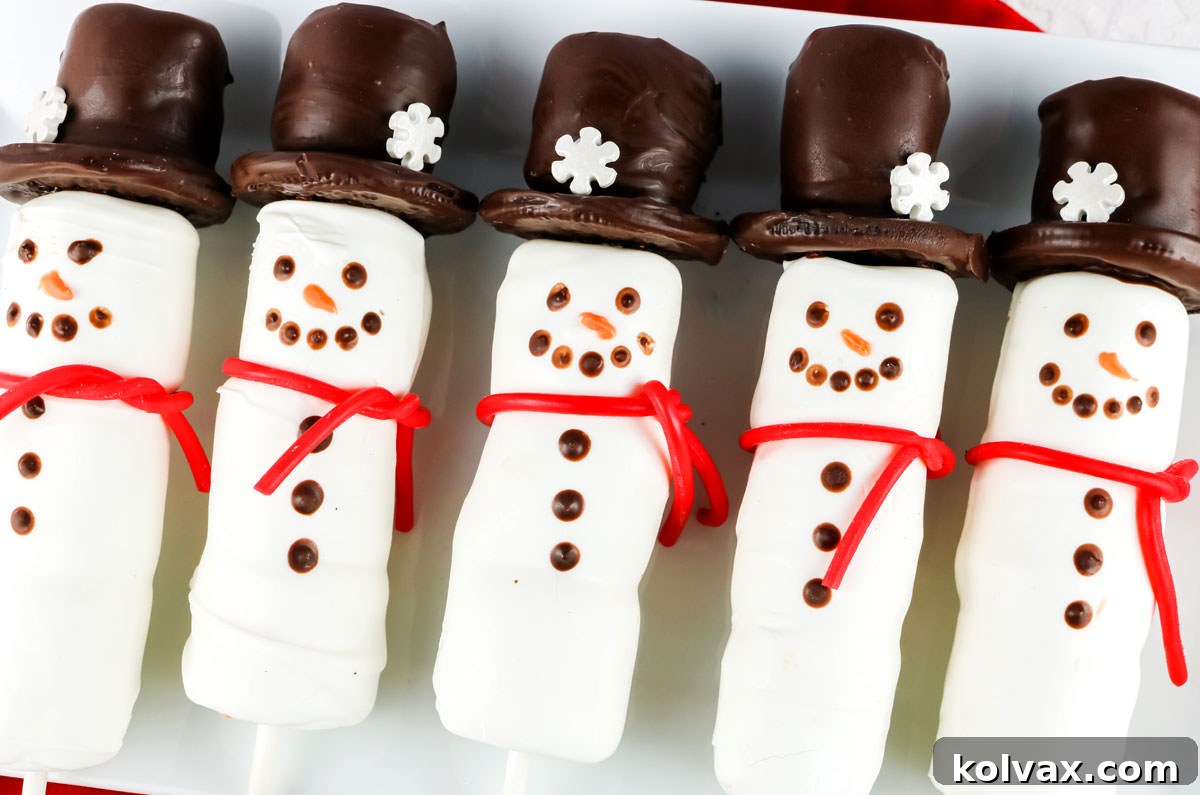 A festive platter of smiling Snowman Marshmallow Pops, each with a candy-coated body and an Oreo cookie hat, ready for a Christmas celebration.