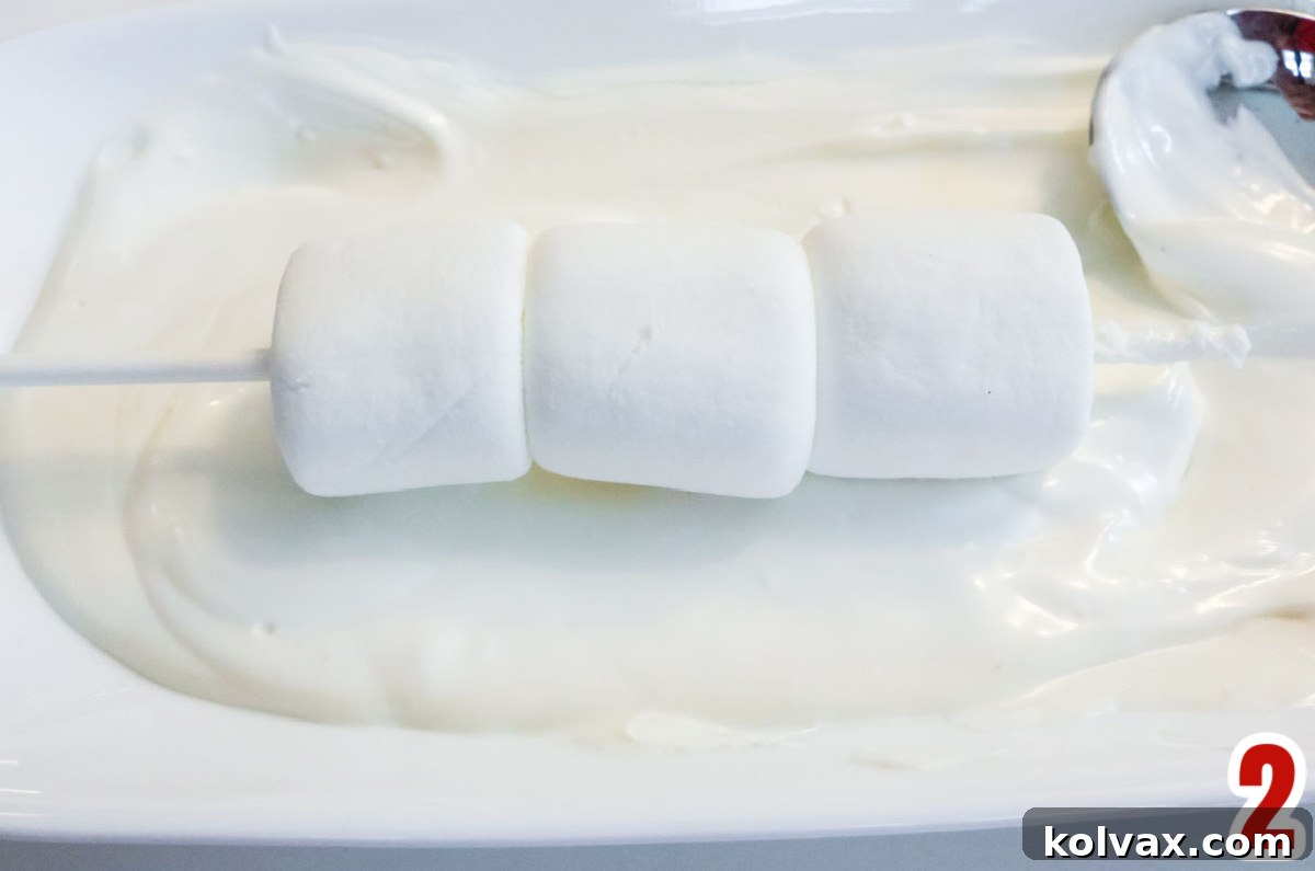 A partially dipped marshmallow pop resting in a pool of smooth, melted white chocolate, showing the coating process.