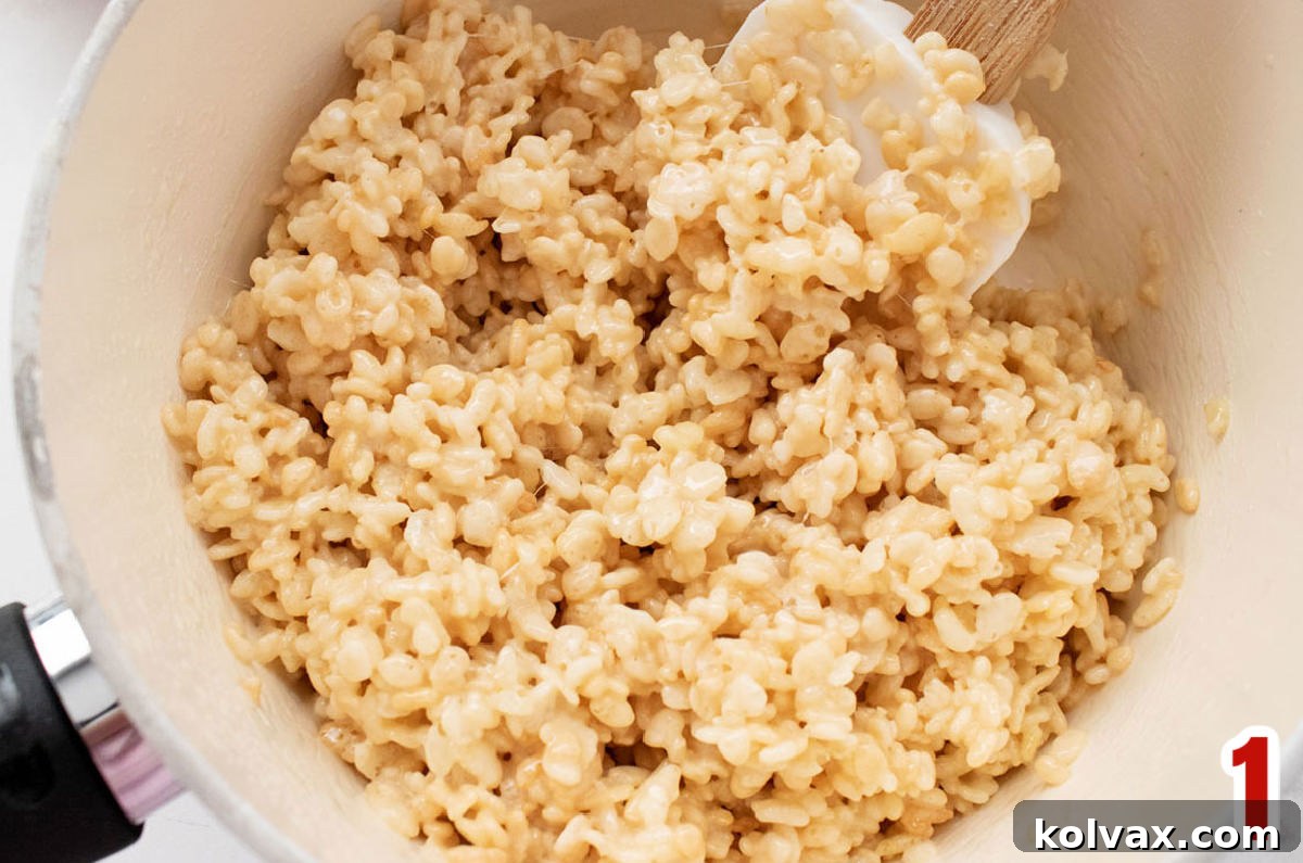 Close-up view of a white saucepan gently warming a golden Rice Krispie Treat mixture, ready for the cereal.