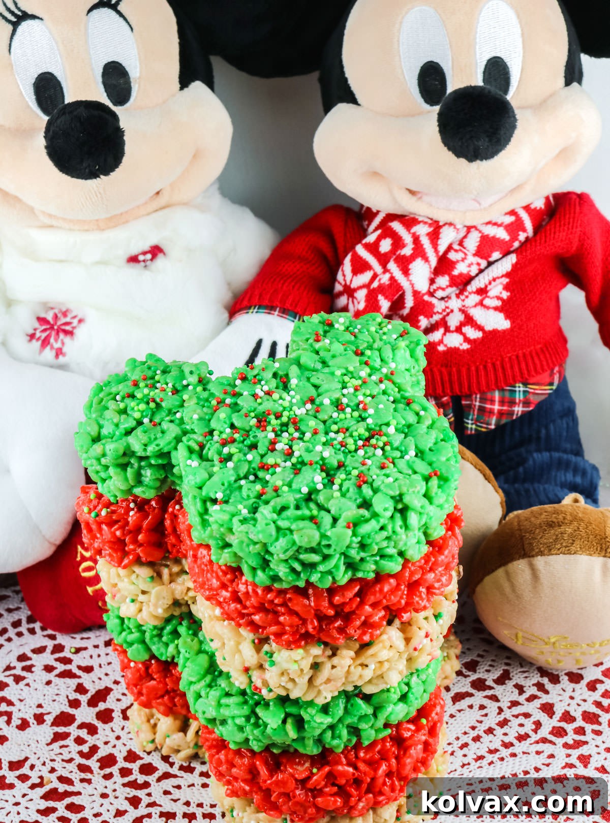 A charming stack of colorful Christmas Mickey Mouse Rice Krispie treats, beautifully arranged in front of plush Mickey Mouse and Minnie Mouse stuffed animals.