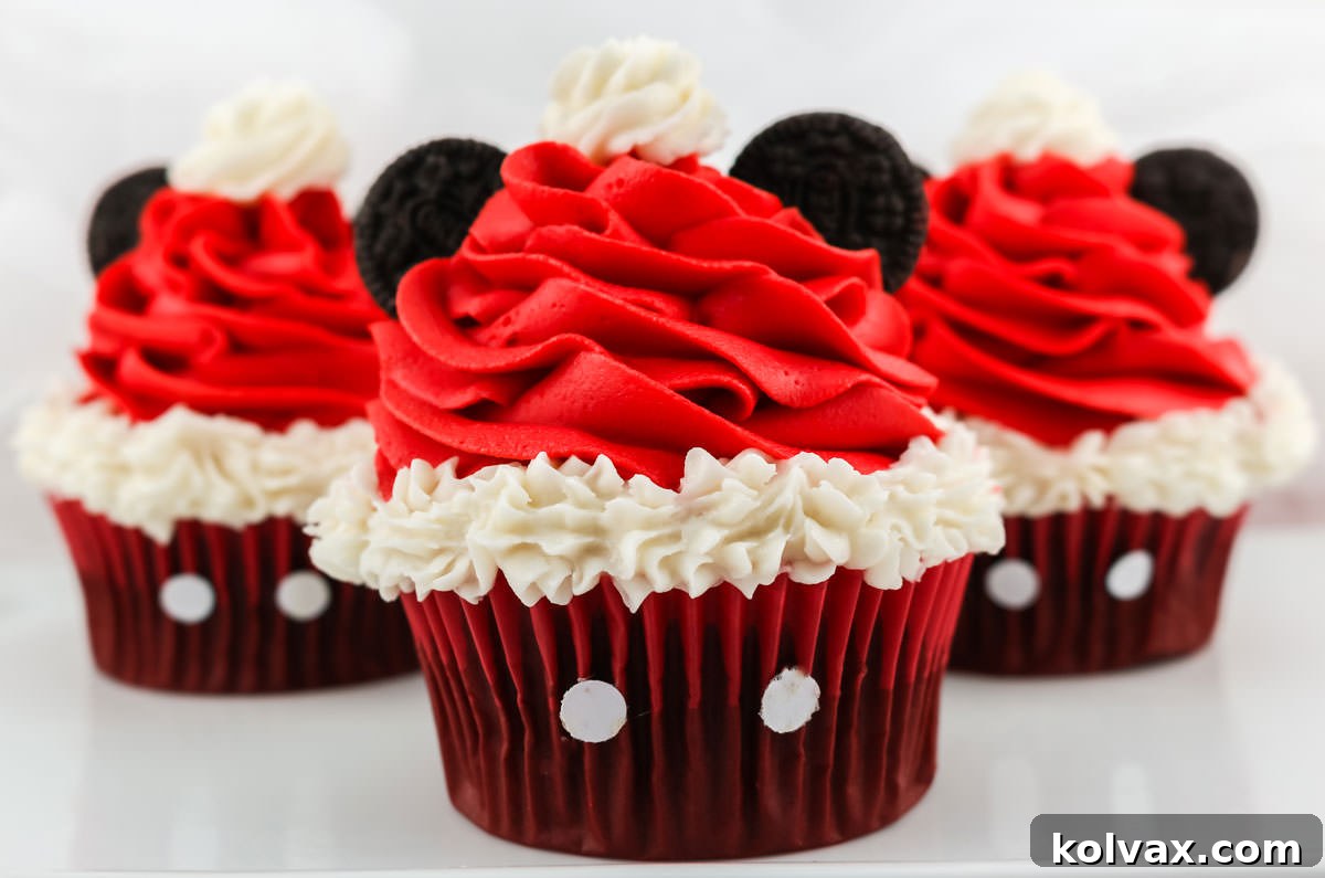 Mickey's Jolly Santa Hat Cupcakes 2 Closeup on three Mickey Mouse Santa Hat Cupcakes sitting on a white table, showcasing their red Santa hats, white fur trim, and Mini Oreo ears.