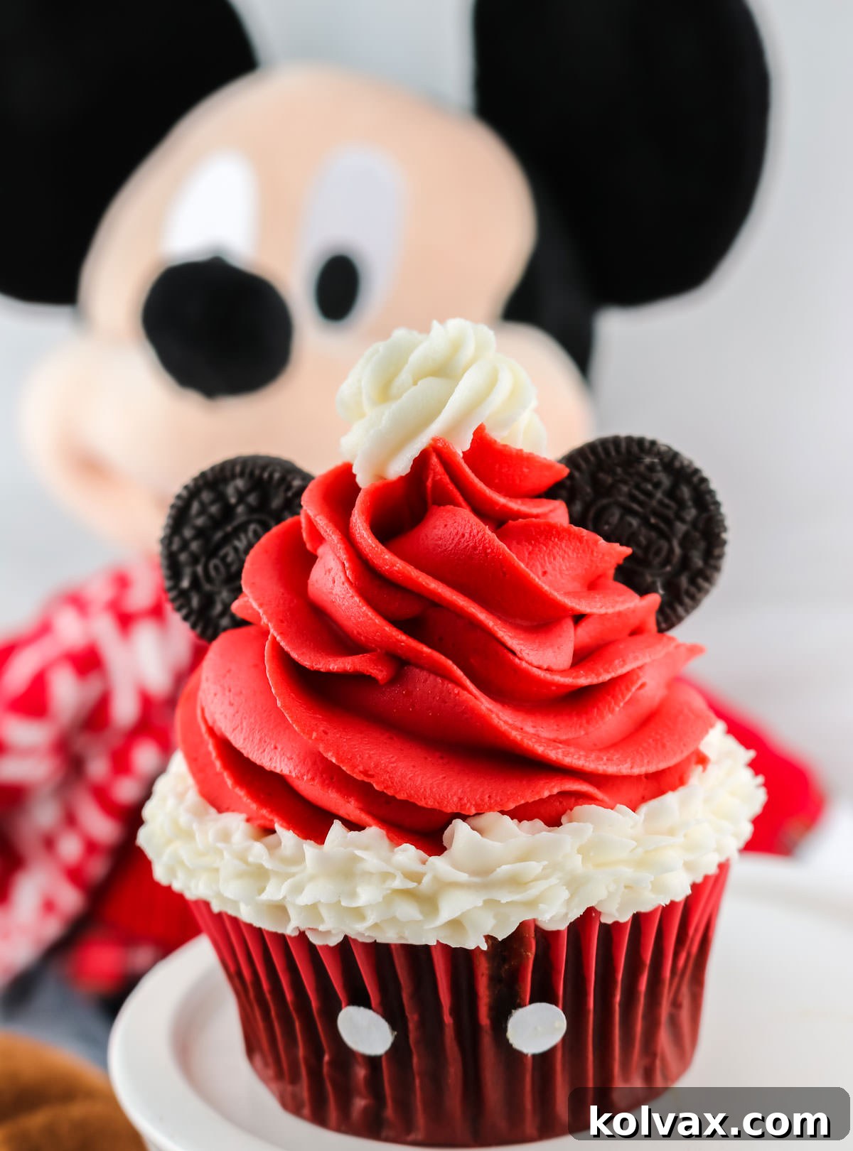 Mickey's Jolly Santa Hat Cupcakes 8 Closeup on a finished Mickey Mouse Santa Hat Cupcake sitting on a white cake plate in front of a Mickey Mouse stuffed animal, ready for enjoyment.
